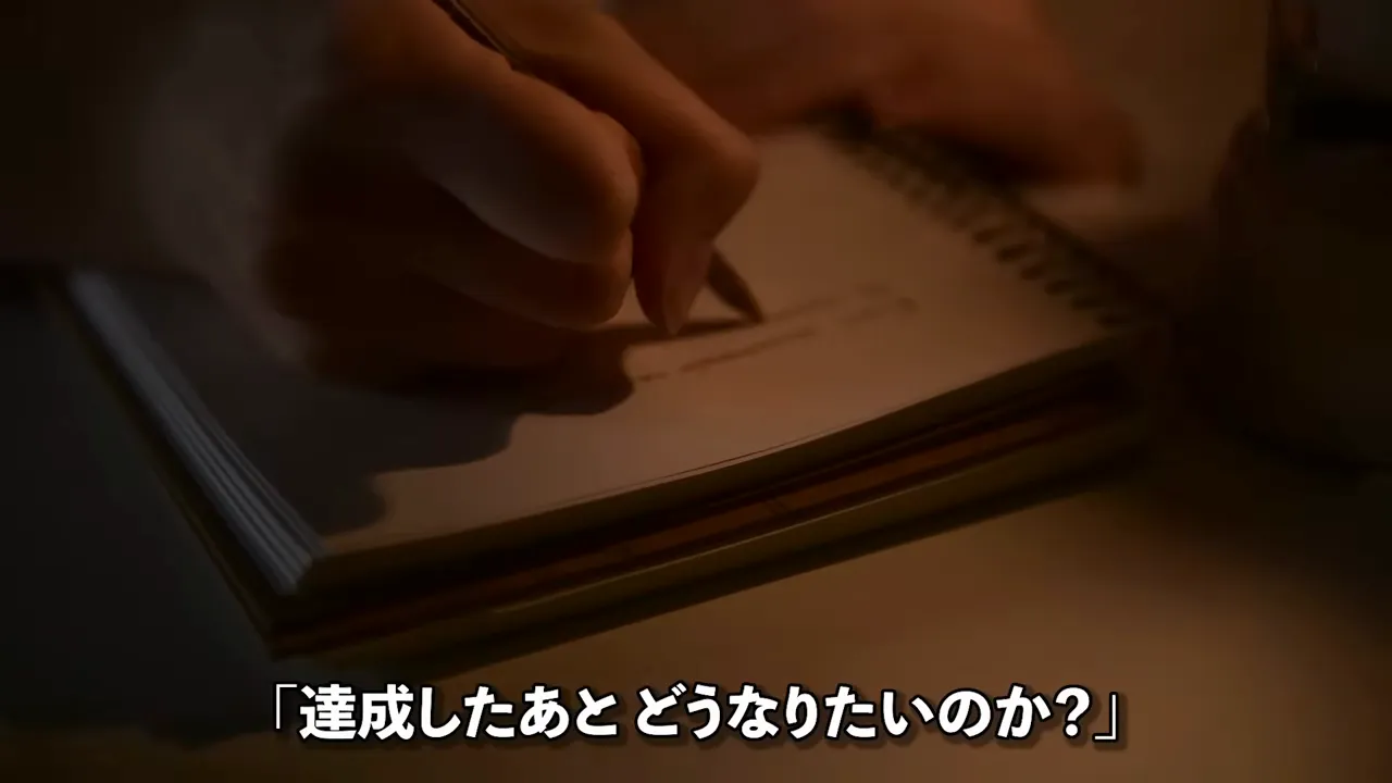 ノートに手書きしている手元と、達成したあとどうなりたいのかという問いが表示された動画の画面